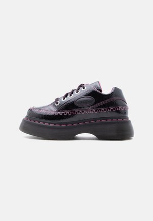 Sort platform sneakers i laklæder med tyk sål, pink syning, snørelukning foran og oval logo-patch på siden, vist i profil.