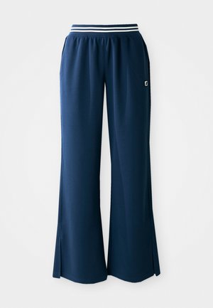 Pantalons de sport bleu marine avec une jambe large, taille élastique, présentant une bande blanche, et fentes latérales pour un mouvement accru. Logo sur la poche.