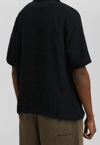 Černá krátká košile z texturované látky s jemným vzorem, s volným střihem a otevřeným límcem.