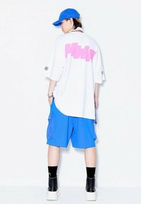 Camiseta blanca de gran tamaño con un estampado gráfico en rosa en la parte posterior, combinada con pantalones cortos tipo cargo azules. Lleva calcetines negros y botas negras robustas.