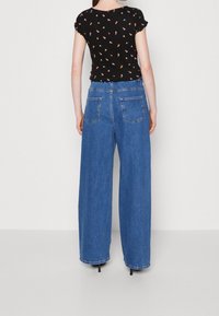 Černý top s krátkým rukávem a květinovým vzorem, který je spárován s širokými džínami modré barvy s retro kapsami a vysokým pasem.