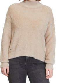 Puffig, beige tröja med hög krage, nedflyttade axlar och en rundad fåll. Har texturerad tyg och subtila detaljer vid fållen.