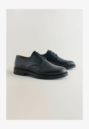 Musta nahkainen pukukenkä, jossa on sileä pinta, pyöreä kärkimalli, nauhat ja tasainen kumipohja. Kahdentyyppiset ompeleet hienovaraisesti esillä.