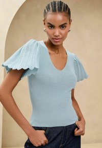 Top tricotat cu un model striat de culoare albastru deschis, cu mâneci tip puff texturate, decolteu în V și o siluetă ajustată. Purtați cu pantaloni din denim închis.