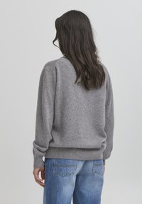 Suéter gris de punto con cuello redondeado y puños acanalados, combinado con jeans de color azul claro. La textura parece suave y acogedora.
