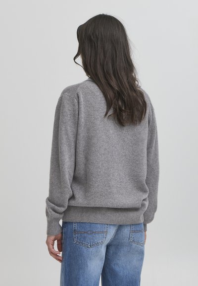 Gray knitted sweater with a rounded neckline and ribbed cuffs, paired with light blue jeans. The texture appears soft and cozy.