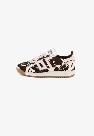 Sneaker a taglio basso con stampa maculata bianca e nera, dettagli rosa, suola marrone chiaro e lacci rosa, mostrato di lato su uno sfondo bianco.