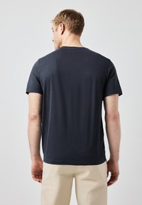 Námořnická modrá bavlněná tričko s krátkým rukávem, jednoduchý design, kulatý výstřih, volný střih a hladká textura. Zobrazena zezadu.