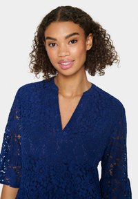 Rochie dantelată bleumarin cu decolteu în V și mâneci 3/4, având modele florale și un finisaj texturat.