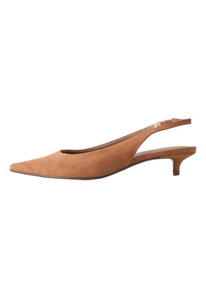 Person iført lyseblå bukser og brune lavhælede spidse slingback-sko, der står på en grå gulv.