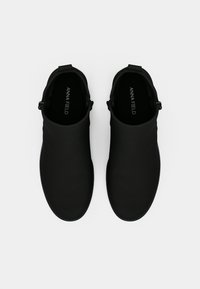 Melnas slip-on kurpes ar gludu, matētu virsmu. Tām ir apaļa pirksta daļa un siksniņa ar regulējamu sprādzi. Iekšpusē redzams zīmola logotips.