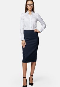 Biała koszula zapinana na guziki z wyprofilowanym kołnierzykiem, zestawiona z dopasowaną granatową spódnicą ołówkową do kolan. Całość uzupełniają czarne sandały na obcasie.