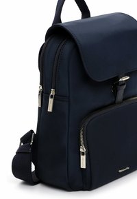 Zaino blu navy con doppie chiusure a cerniera, texture liscia, tasca frontale con zip e tracolla regolabile. Dettaglio di hardware con marchio visibile.