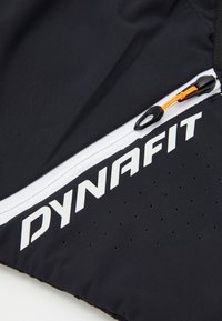 Tessuto sportivo nero con logo "DYNAFIT" bianco. Presenta una tasca con zip e pull tab arancione, oltre a piccole perforazioni lungo il bordo.