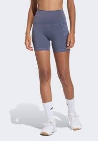 High-waisted, fitted athletic shorts in slate blue fabric, featuring flat seams and a smooth texture, paired with white athletic shoes and socks.