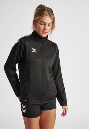Zwarte softshell jas met hoge kraag, rits aan de voorkant en zijzakken; beschikt over een wit logo en schouderaccenten in contrasterend wit.