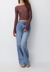Spidsblonde crop top i mørk mauve med lange ærmer og scallop-kant; parret med lyseblå wide-leg jeans; grå fodtøj.