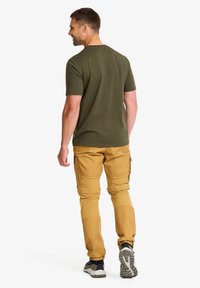 Olivgrön t-shirt och cargo-byxor i senapsgul. Byxorna har dragkedjefickor; t-shirten har en klassisk halsringning och korta ärmar.