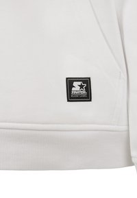 Ourlet d'un vêtement blanc avec une étiquette carrée noire affichant une étoile blanche et la marque "Starter Black Label".