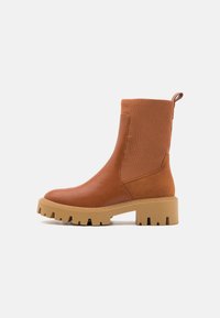 Botas de tobillo marrones con un cuerpo de cuero suave, parte superior de textil acanalado y suela de goma gruesa con un patrón de tracción.