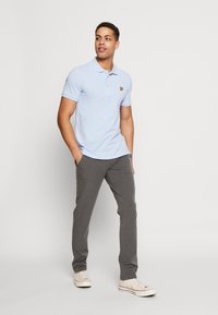 Light blue polo shirt with short sleeves and a yellow logo, paired with gray trousers and white sneakers. Simple design with a classic fit.