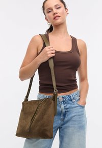 Borsa a tracolla in suede marrone con tracolla in pelle verde, forma rettangolare, dettaglio con cerniera e superficie liscia.
