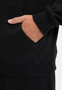Felpa nera con cappuccio, dotata di tasca frontale e polsini a coste. Tessuto morbido, design casual con dettagli minimi. Adatta per l'uso quotidiano.