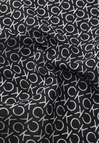 Tessuto nero con un motivo ripetuto di logo bianco. La texture appare liscia, con una leggera lucentezza nella trama.