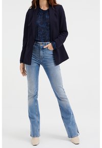 Marinblazer över en mönstrad blå blus, kombinerad med ljusblå utsvängda jeans och krämfärgade klackskor. Enkelt och skräddarsytt design.