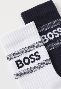 Bavlnené ponožky v bielej a námorníckej modrej farbe s rebrovanými elastickými manžetami a horizontálnymi pruhmi, na ktorých je logo "BOSS". Hladká textúra a priliehavé uloženie.