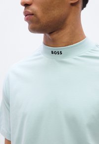 Ανοιχτό μπλε κοντομάνικη μπλούζα με ριμπ γιακά. Η λέξη "BOSS" είναι τυπωμένη με μαύρο στο γιακά. Λείο υλικό, casual σχέδιο.