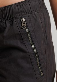 Zwarte broek met een elastische tailleband en een zijritszak. Heeft een zachte stofstructuur en een slim fit ontwerp.