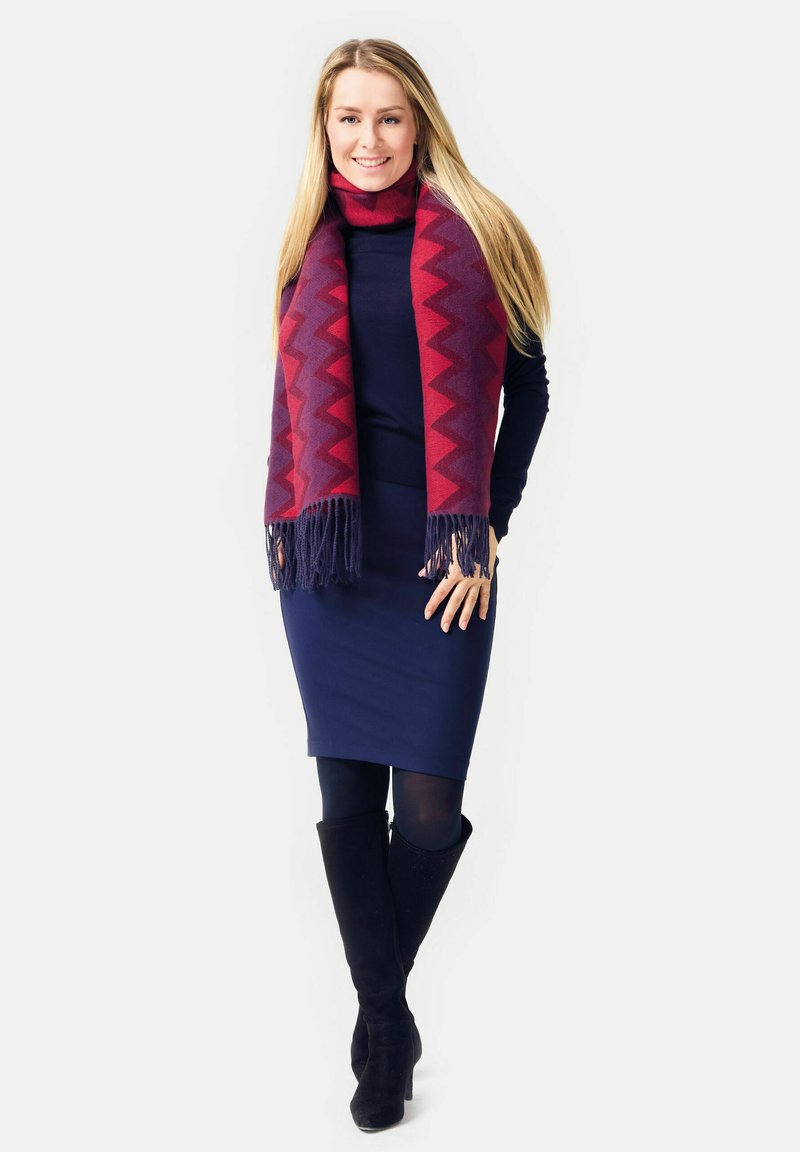Maroon and purple zigzag-patterned scarf layered over a dark navy long-sleeve top and fitted skirt, paired with knee-high black boots.