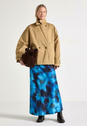 Beige bomullsskjorta med dubbelknäppt design, kombinerad med en lång blå och svart tie-dye kjol och brun mockaväska. Svarta ankelboots.