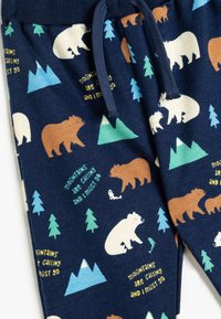 Pantalones de chándal azul marino con un estampado de osos, montañas y árboles. El material es suave con un acabado texturizado; incluye una cinturilla con cordón.