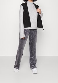 Grå fleece-tröja kombinerad med en svart ärmlös väst och grå velourbyxor. Vita sneakers fulländar outfiten. Sura texturer, avslappnad passform.