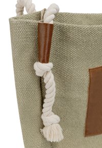 Zielona torba typu tote, tkana, z brązowymi skórzanymi akcentami, kremowymi skręconymi uchwytami i teksturowaną powierzchnią. Wyrazisty detal w postaci węzła i frędzli.