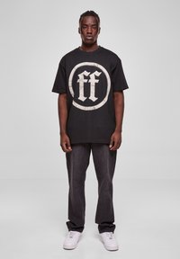 Black t-shirt with a large circular graphic in light gray featuring "ff" in the center, paired with dark gray jeans and white sneakers.