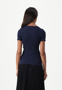 Navy ribbed top yang pas dengan lengan pendek, tepi bergelombang di hem dan lengan, dipadukan dengan rok plisket hitam.