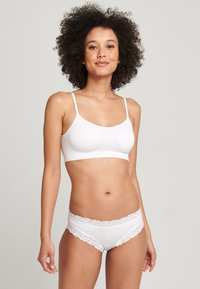 Vit bralette med tunna axelband och slät tyg, i kombination med vita trosor med spetskant som visar en mjuk, sömlös design.