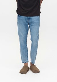 Ljust blå denimjeans med tapered passform, som har fem fickor och subtila slitningar. Bärs med bruna slip-on skor.