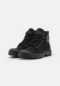 Botas altas negras con suela de goma, diseño de cordones, cuello acolchado y un parche de logo redondo en el lateral. Parte superior de tejido texturizado.