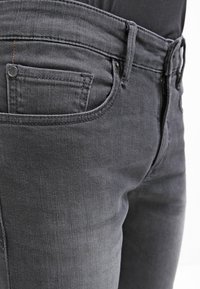 Mörkgrå denimjeans med slim fit. Funktioner inkluderar en liten framficka, standard midjehöjd och metallknappsstängning.