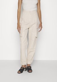 Beiga cargobyxor med elastiska muddar, två sidofickor och hög midja. Matchas med svarta remsandaler med klack.