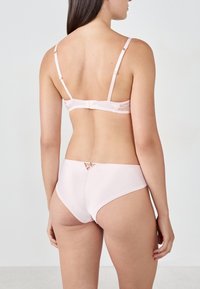 Reggiseno rosa chiaro e slip abbinati realizzati in tessuto liscio. Il reggiseno presenta spalline regolabili e una chiusura a gancio; gli slip hanno un taglio decorativo.