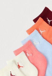 Έγχρωμες βαμβακερές κάλτσες με ριμπ μανσέτες, παρουσιασμένες σε βαθμιαία μετάβαση από σκούρο κόκκινο, ροδάκινο, ανοιχτό μπλε, ροζ έως λευκό με λογότυπα.