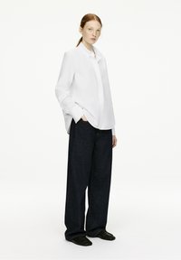 White collared shirt with a loose fit, paired with dark blue denim wide-leg pants. Smooth fabric texture, with black slip-on shoes.