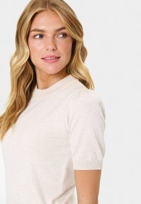 Ljus beige kortärmad tröja med ribbad rund halsringning och subtila puffärmar, tillverkad av mjukt, texturerat tyg.