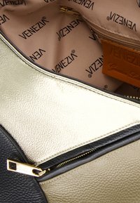 Czarna i złota torba z teksturowanej skóry. Posiada gładki zamek z złotymi elementami. Wnętrze ma beżową podszewkę z powtarzającym się brandingiem.