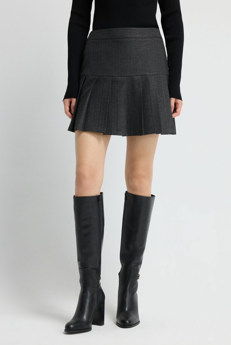 Grijze geplooide rok met een gestructureerde stof, gecombineerd met kniehoge zwarte leren laarzen met ritsluiting en blokhakken.